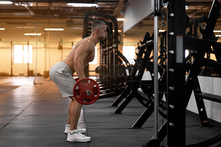 肌肉运动健美运动员健身模型站在镜子前背对着镜头训练升降杠铃室内健身房