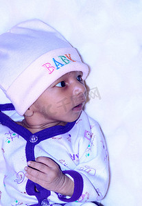 穿着冬装的可爱印度新生男婴的特写美丽肖像侧身看着，感到好奇，并摆出一副惊奇的样子。
