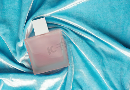 粉红色的满瓶装着磨砂玻璃香水，躺在蓝色的背景上