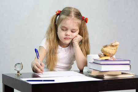 女孩在一张纸上写字，坐在图像作家的桌子旁
