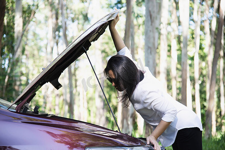 地道摄影照片_亚洲女性打电话给修理工或保险人员，以解决当地道路上的汽车发动机问题