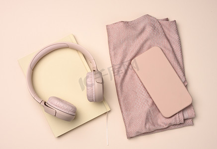 粉色背景中的一双粉色运动鞋、无线耳机、智能手机和智能手表