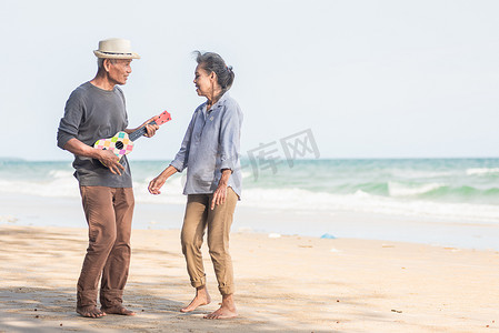 快乐的老年夫妇在阳光明媚的海边海滩放松，在户外唱歌和弹吉他