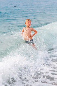 小男孩海边摄影照片_快乐的小男孩在海边的海浪中玩得开心