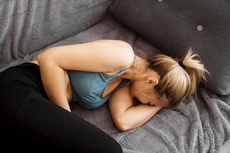 肚子痛摄影照片_家中沙发上肚子痛的妇女的侧视图