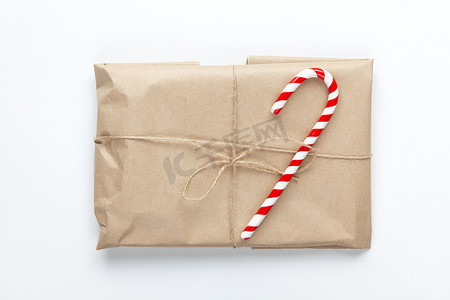 赶车鞭子摄影照片_用牛皮纸包裹的圣诞礼物，系着鞭子，在白色背景上装饰着甘蔗糖。