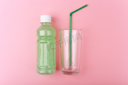 亮粉色背景中带绿色吸管的空玻璃旁边是带浅绿色排毒饮料的透明瓶子