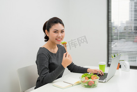 女人在现代办公室内部享用健康的商务午餐。