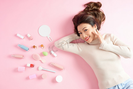 快乐的亚洲女人躺在粉红色的地板上，拿着她的化妆工具。