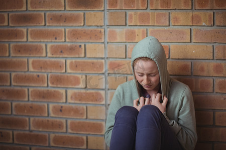 悲伤的女学生独自坐在砖墙上