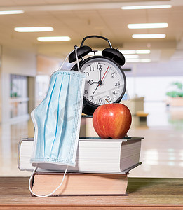 回到学校背景概念，包括一摞书、闹钟、带面罩的苹果