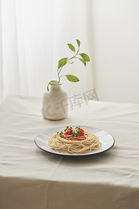 食物、白盘中的肉酱意大利面和准备好的白色桌子上的一瓶植物