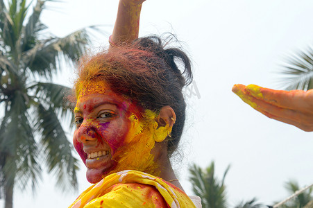 在 Holi 色彩节期间，一位年轻的印度快乐女人的肖像，脸上涂着粉红色、黄色和红色的 Holi 彩色粉末涂料。