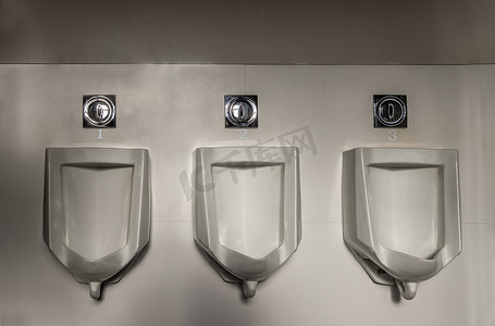 厕所标语冲水摄影照片_男卫生间三个白色分离式小便池特写及自动红外线冲水，卫生间男用白色陶瓷小便池设计。