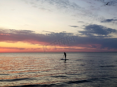 一个人在 SUP 上的剪影，站起来桨板，以海上彩色日落为背景