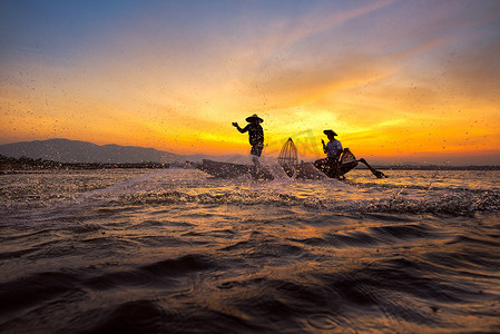 亚洲渔民在木船上撒网，在日出前的清晨在自然河流中捕捞淡水鱼。