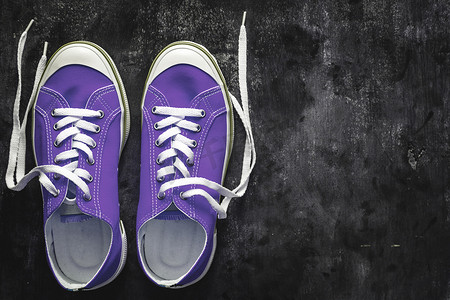 黑暗系背景摄影照片_紫色-粉红色-淡紫色运动鞋，在深色混凝土背景上系有解开的鞋带。