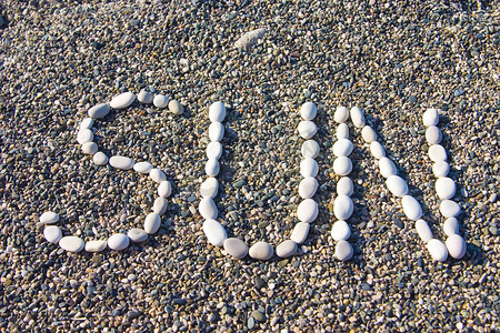 沿海鹅卵石背景上用白色石头制成的“太阳”一词