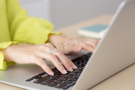 在家庭办公室的办公桌上使用笔记本电脑工作的手年轻亚洲女商人的特写，自由职业者在桌上的笔记本上看和打字，在线学习的女性，商业和教育概念。