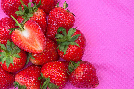 纯红摄影照片_表面布满种子的草莓甜红果粉红色织物上红莓心形水果的特写质地