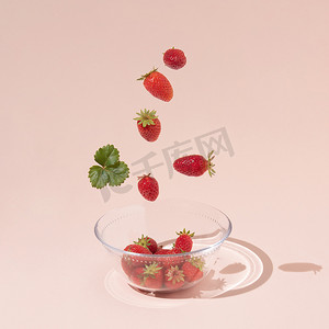 夏季水果创意摄影照片_新鲜的夏季水果、草莓和绿叶落入玻璃碗中，与粉红色背景隔离。