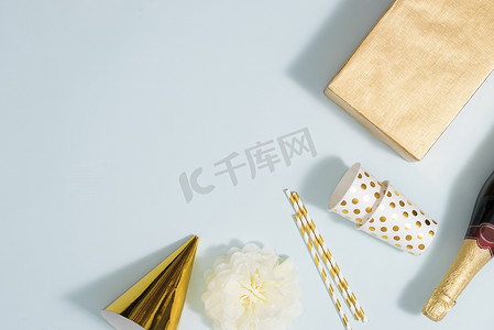 平躺式圣诞或派对背景，配有礼品盒、香槟酒瓶、蝴蝶结、装饰品和金色包装纸。