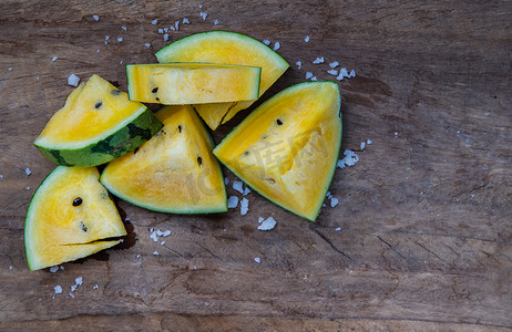 黄色西瓜摄影照片_新鲜多汁的黄色西瓜在旧木背景上切成三角形。