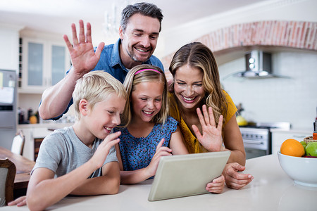 父母和孩子在使用数字平板电脑进行视频聊天时挥手