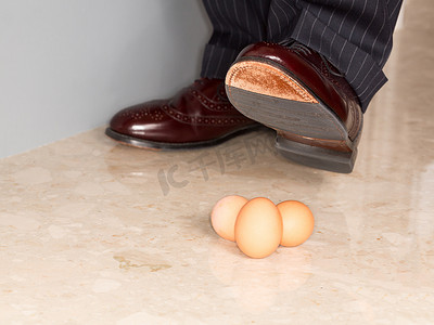 小心压脚摄影照片_男人的鞋子踩在三个鸡蛋上