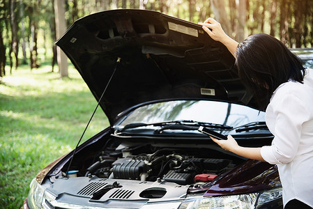 亚洲女性打电话给修理工或保险人员，以解决当地道路上的汽车发动机问题
