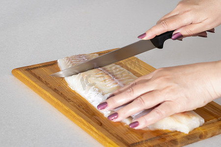 女手在砧板上用刀切鱼肉。