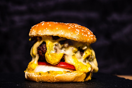 新鲜美味牛肉芝士汉堡的细节与黑色背景中突显的融化奶酪