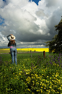 农场门口的乡村女人看着金色庄稼和田野上空的云彩