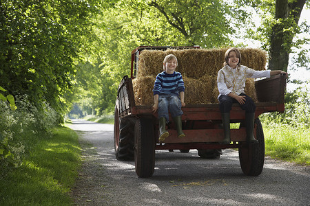 儿童拖车摄影照片_两个小男孩的全长肖像坐在乡间小路上的拖车后面