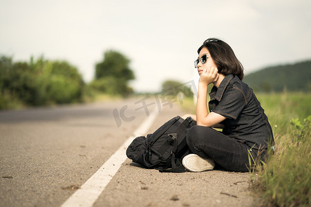 女人背着背包坐在乡下的一条路上搭便车