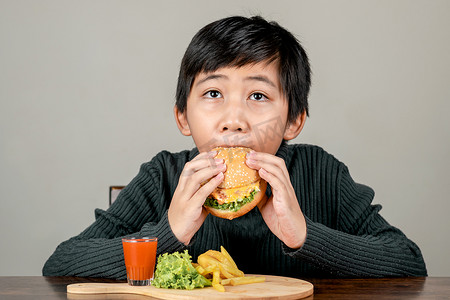 男孩吃汉堡摄影照片_可爱的亚洲男孩开心地吃着美味的汉堡