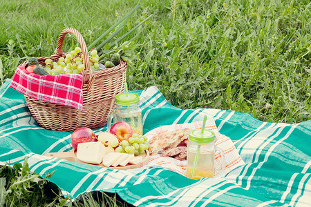 夏日在草地上野餐 — 篮子、葡萄、奶酪、面包、苹果 — 夏季户外休闲的概念