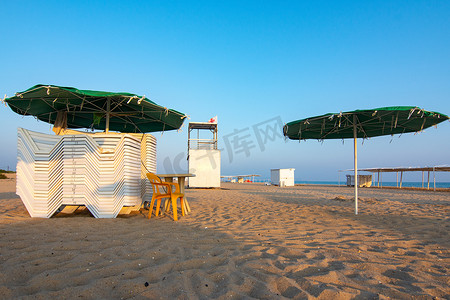 日落时，折叠的日光浴躺椅和一个空荡荡的救生员岗位在荒凉的沙滩上