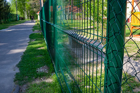 涂成绿色的金属栅栏。公园操场沿线的金属丝光栅