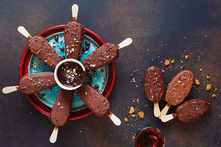 冰淇淋设计摄影照片_巧克力覆盖的冰淇淋在乡村背景上粘着牛奶和黑巧克力。