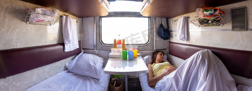 预留座位火车车厢内部的全景图，一个女孩睡在较低的架子上
