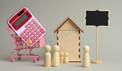 金融人物摄影照片_木制人物家庭和房屋背景上的房地产经纪人，以及灰色背景下手推车中的计算器
