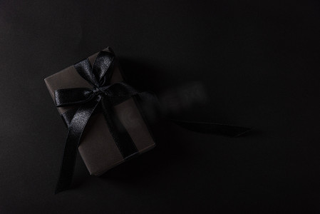 丝带盒摄影照片_在黑纸和黑弓丝带包裹的礼物盒