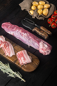 黑色木桌背景上的有机猪肉片，配有烧烤或烘焙用配料和香草、鼠尾草、马铃薯