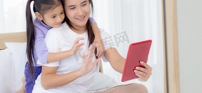 微信语音通话中摄影照片_年轻的亚洲妈妈和女儿在平板电脑上视频通话与家人一起问候，快乐的母亲和女孩使用技术与互联网在线交流，两个人。