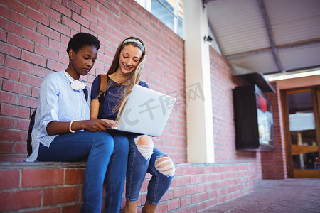 坐在砖墙上使用笔记本电脑的女学生