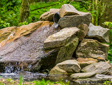 装饰小简单的摄影照片_花园中用巨石制成的小瀑布，简单而美丽的花园建筑，池塘装饰，自然背景