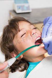 牙医椅摄影照片_儿科牙医在牙医椅上检查小男孩的牙齿