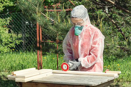 呼吸器、护目镜和工作服的女木匠用角磨机处理一块木板
