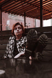 长腿桌子摄影照片_酒吧里红短发的年轻女人把腿放在桌子上
